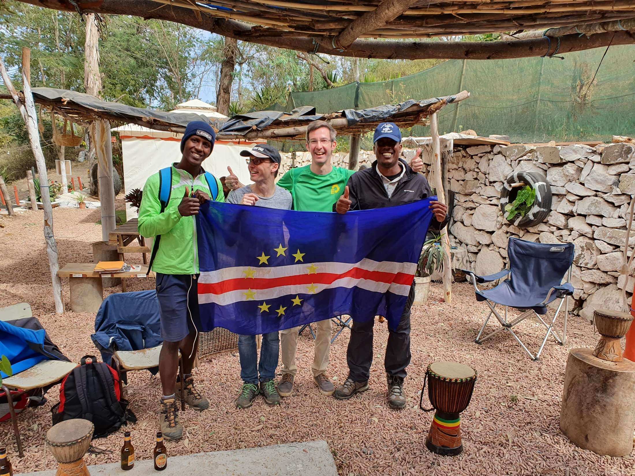 Santiago: Vier Wanderer halten in der Snackbar Lemba Lemba eine Kapverden-Flagge in die Kamera